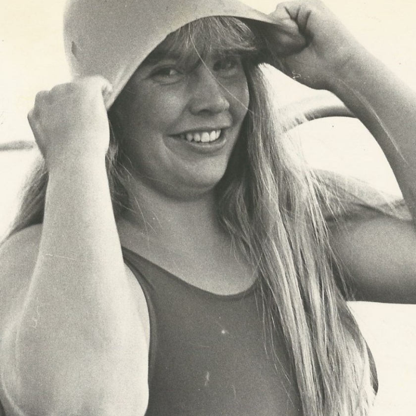 Faded photo of Lynne Cox, smiling, wearing a swimsuit, and pulling a swim cap over her head.