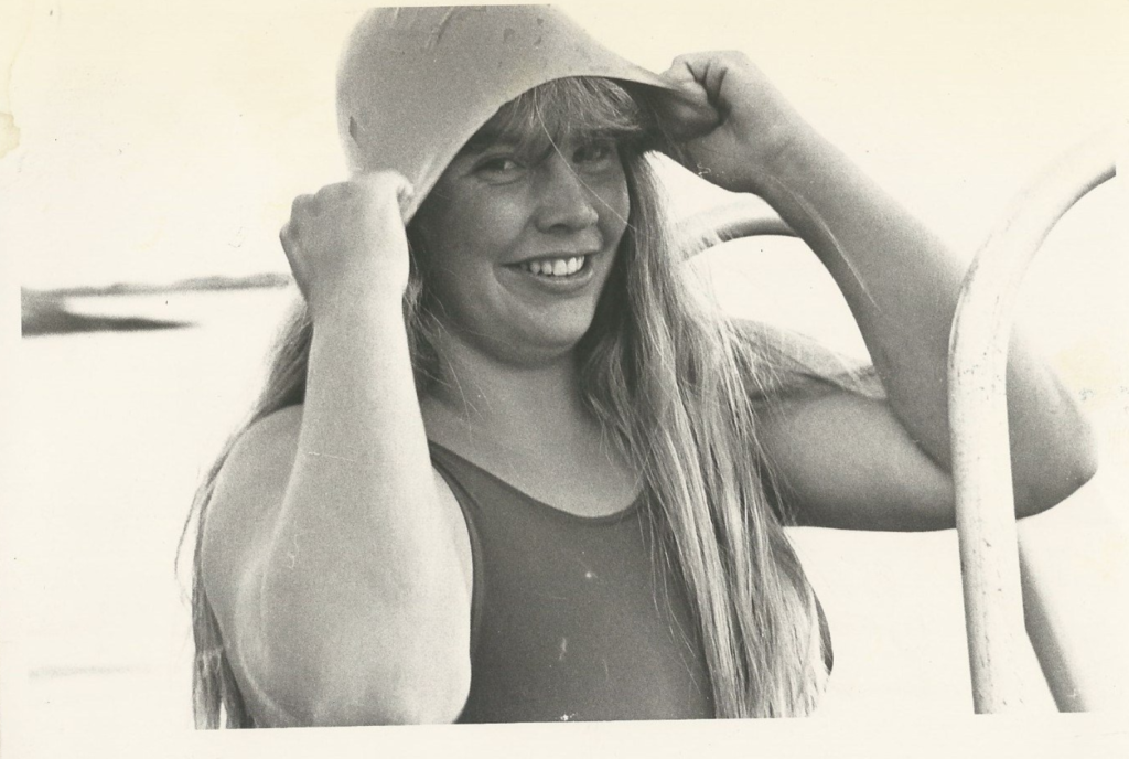 Faded photo of Lynne Cox, smiling, wearing a swimsuit, and pulling a swim cap over her head.