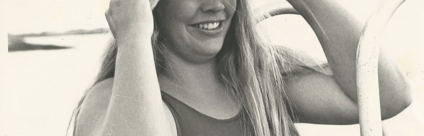 Faded photo of Lynne Cox, smiling, wearing a swimsuit, and pulling a swim cap over her head.