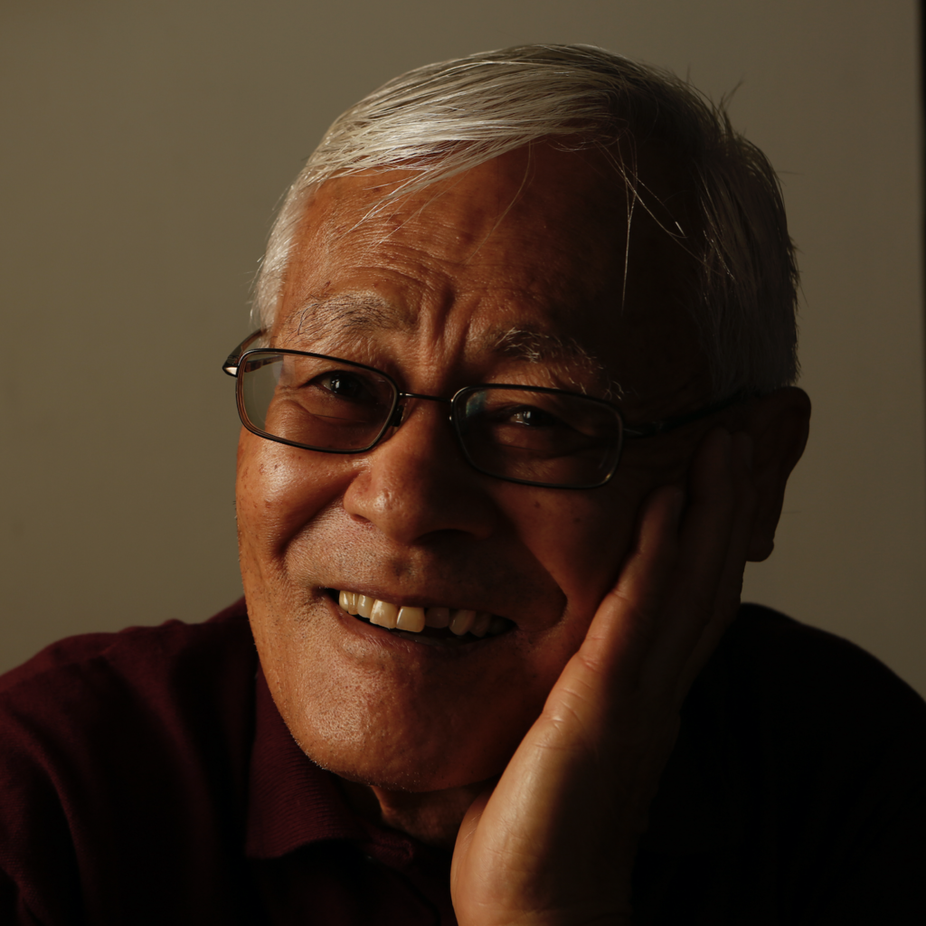 Close-up portrait of Shigeru Yabu, smiling, resting his cheek in his hand.