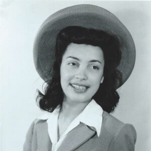 Black and White portrait photo of a young Betty Reid Soskin smiling, and wearing a hat and a suit. with
