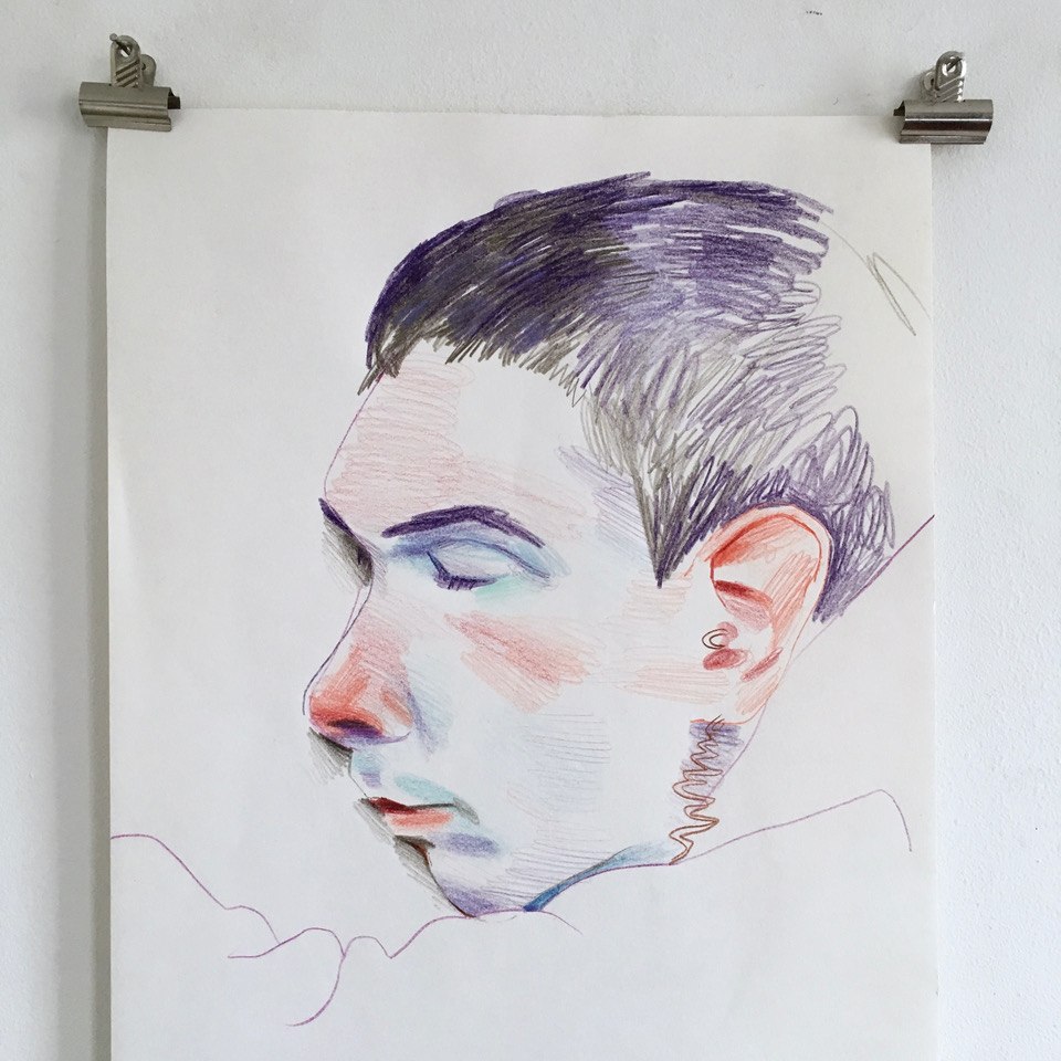 Photograph of a drawing pinned up on a wall. The drawing shows the head and face of a young man asleep in profile—the ears, nose, lips, and cheeks are accented with red and the eyelids and upper lip are accented with blue. The man has cropped dark hair, pale skin, and an earring.