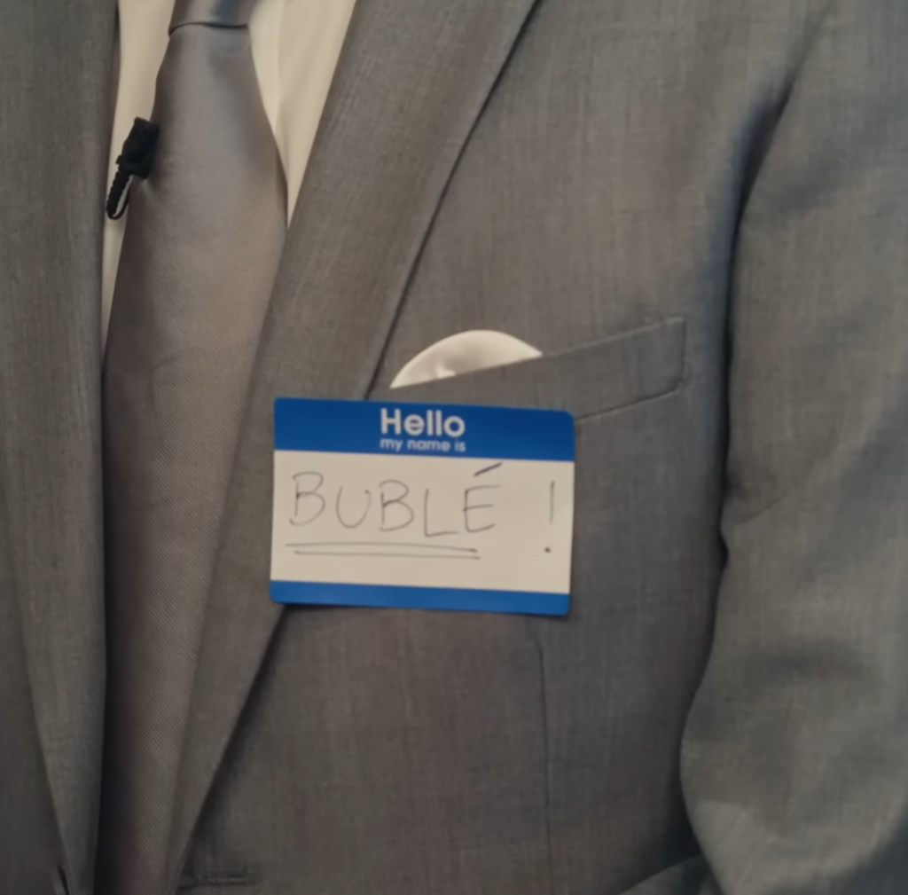 A blue and white name tag on a gray suit jacket that reads "Hello, my name is" and Dan Perlman has written underneath BUBLÉ in all capital letters, with an exclamation point, and underlined.