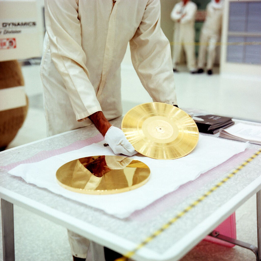 Color photograph of someone wearing a white jumpsuit and white gloves handling the golden record
